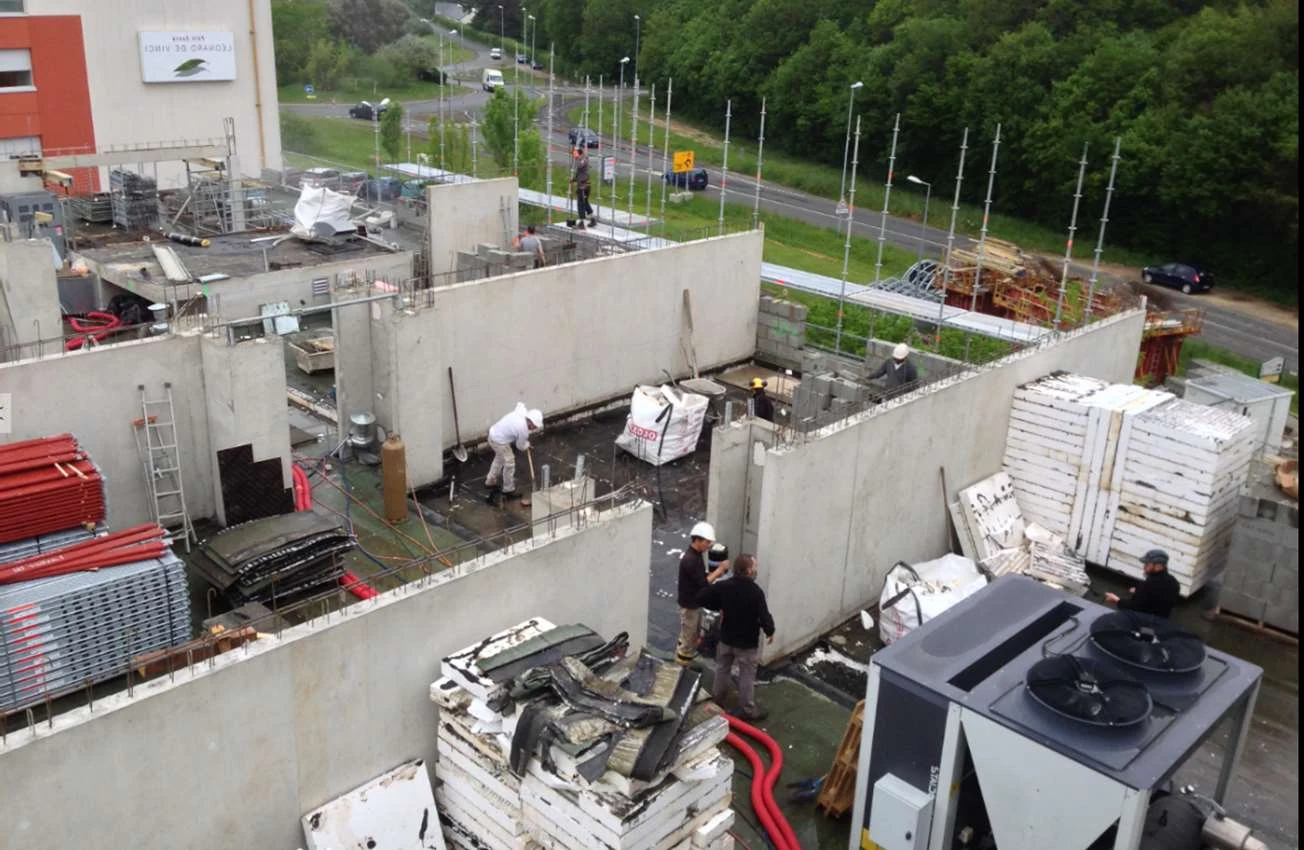 Photo du chantier en cours : surélévation visible depuis les toits, équipements de la clinique en fonctionnement au-dessous, échafaudages et matériaux périphériques